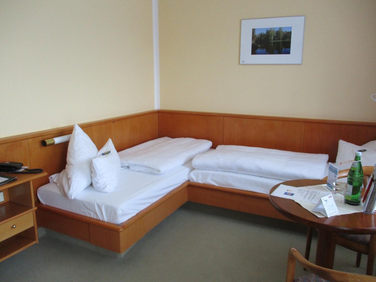 A hotel room with a wooden bed, a bedside table with a lamp, and a framed picture on the wall.