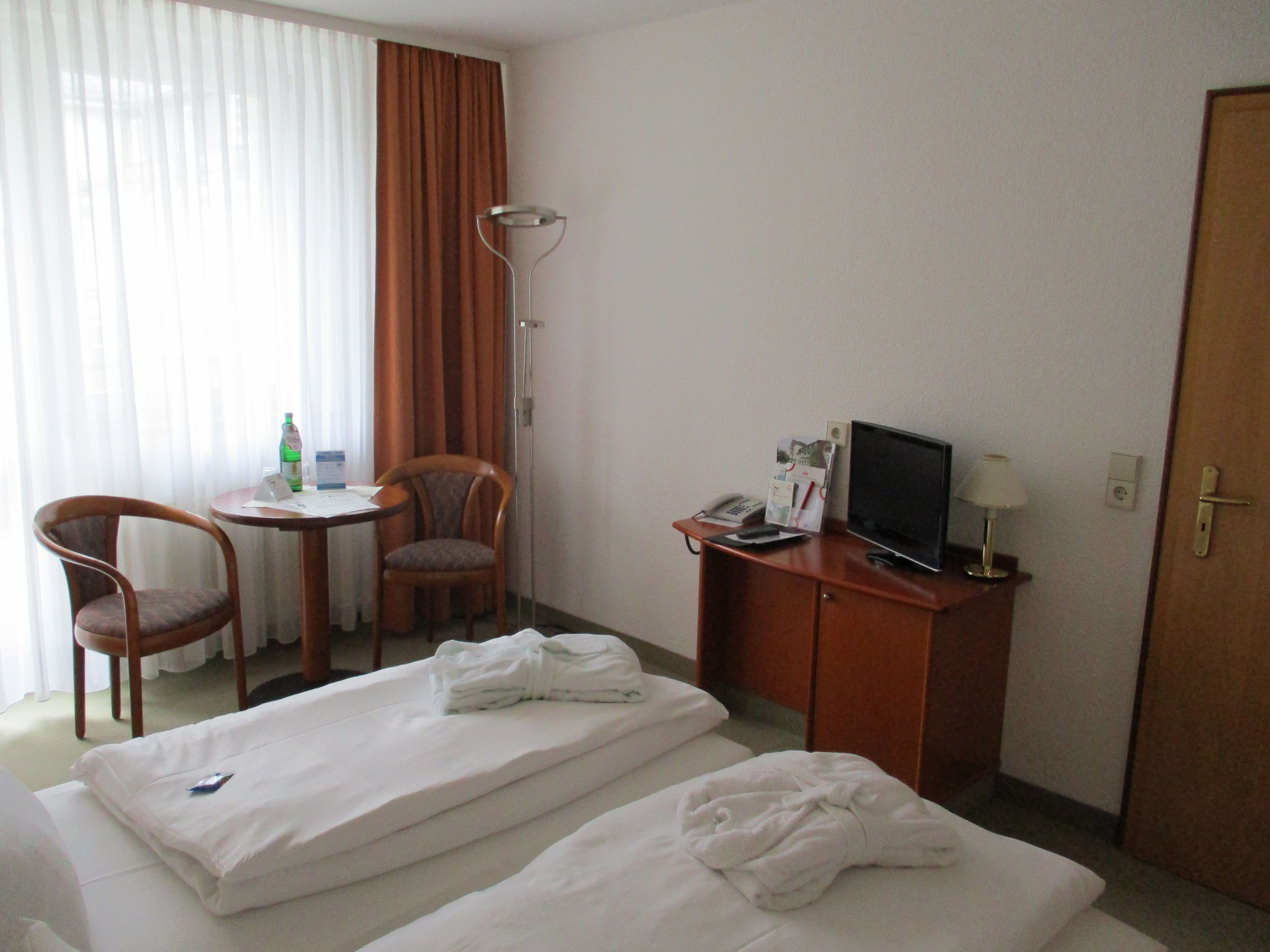 A hotel room with two beds, a desk with a chair, a television, and a lamp.