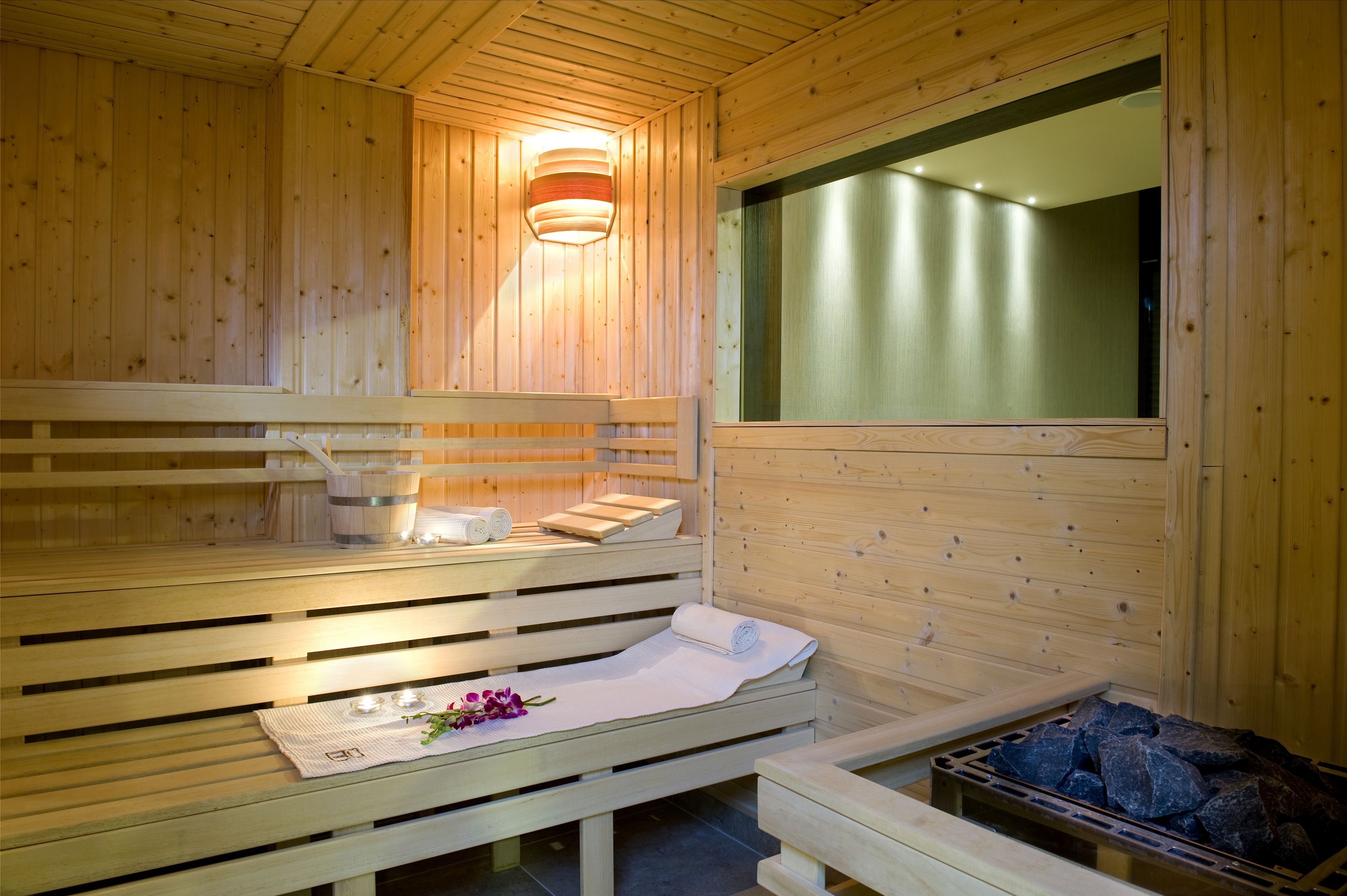 A wooden sauna with benches, a large window, and a stone heater.