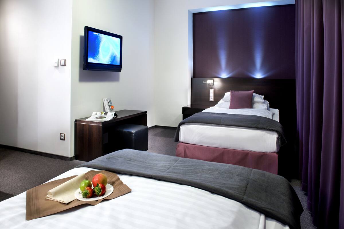 Quarto de hotel com duas camas, televisão, escrivaninha e bandeja com frutas.