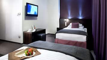 Ein Hotelzimmer mit zwei Betten, einem Fernseher, einem Schreibtisch und einer Platte mit Früchten.