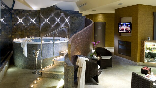 Un moderno espacio de spa con una escalera curva, una bañera de hidromasaje y un área de descanso con mobiliario de mimbre.