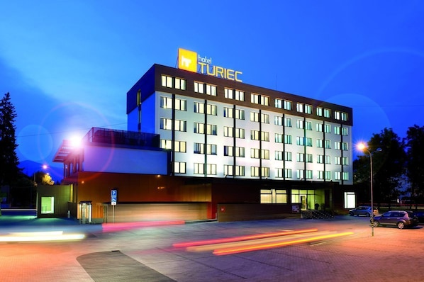 A modern hotel building with a prominent sign, multiple floors, and a parking area.