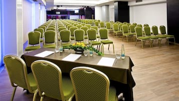 A conference room with rows of green chairs and tables, equipped with water bottles and notepads.