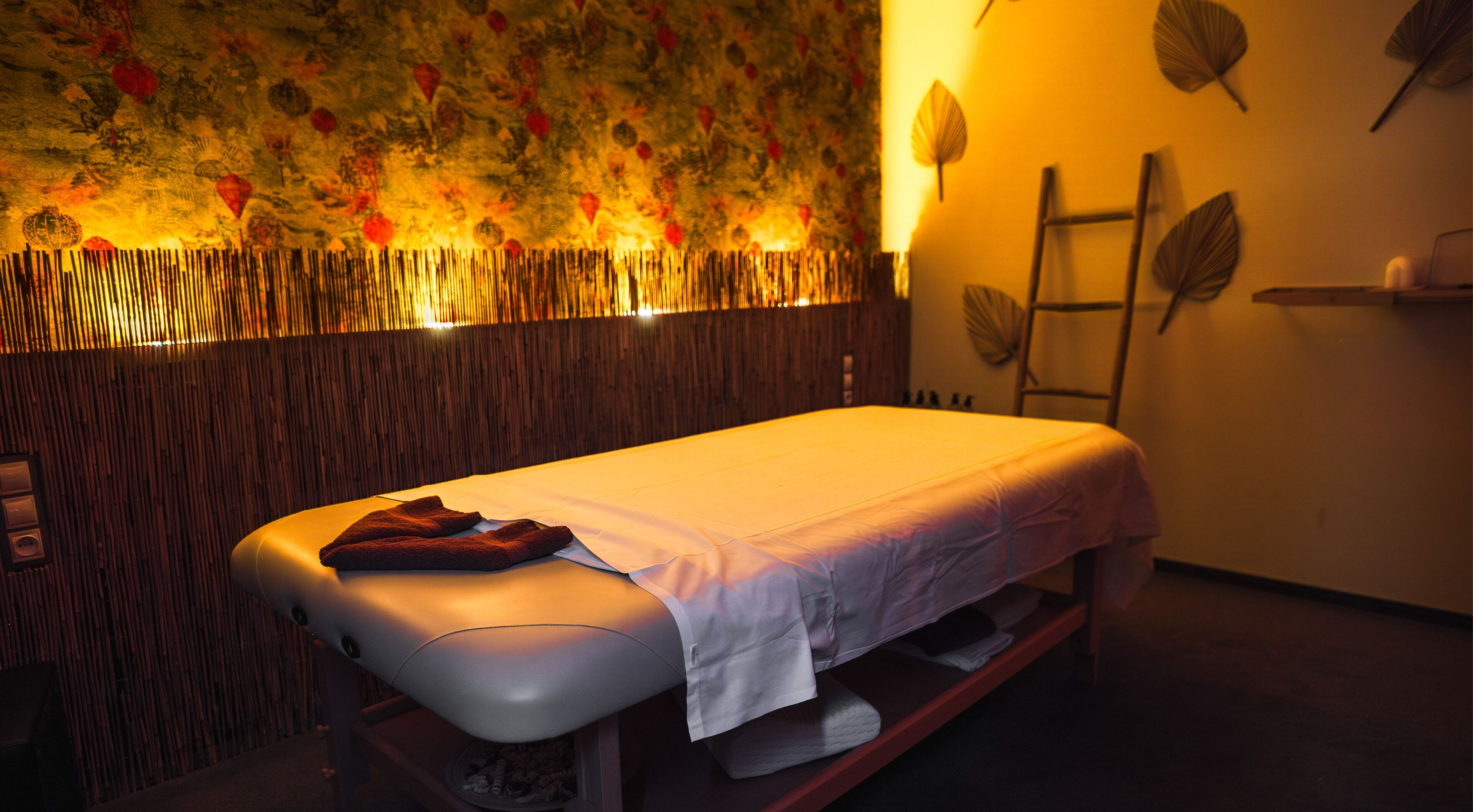 A room with a massage table, a wooden wall with a leaf pattern, and a ladder against the wall.