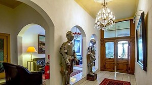 A hallway with arched doorways, a chandelier, a red patterned rug, and two metallic statues. - Hotel Adler (Ingolstadt)