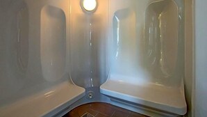 A corner of a bathroom with two white bathtubs, a round mirror, and a light fixture on the ceiling. - Hotel Adler (Ingolstadt)