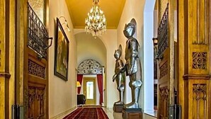 A grand hallway with a chandelier, wooden doors, and a red carpet leading to a room with a red door. - Hotel Adler (Ingolstadt)