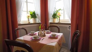 A dining area with a table set for four, two potted plants, and a window with sheer curtains. - Hotel Adler (Ingolstadt)