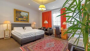 A hotel room with two beds, a desk, a chair, a red rug, a painting, and a large window with curtains. - Hotel Adler (Ingolstadt)