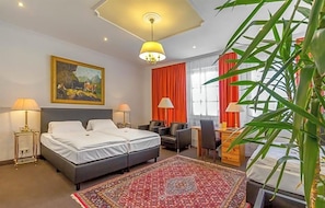 A hotel room with two beds, a desk, a chair, a red rug, a painting, and a large window with curtains. - Hotel Adler (Ingolstadt)