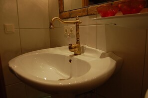 Ett badrum med ett vitt handfat, en guldbrun kran och en spegel ovanför.