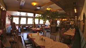 A restaurant with multiple tables and booths, wooden ceiling beams, and large windows allowing natural light. - Hotel Schweizerhof (Wildschönau)