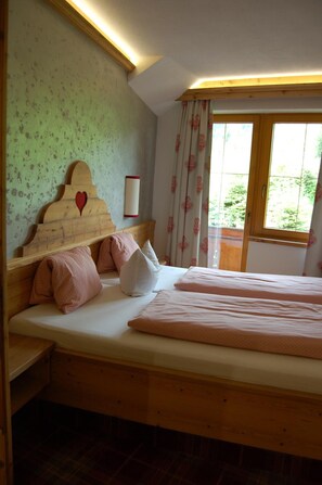 A bedroom with a wooden bed, a headboard with a heart-shaped cutout, and a window with curtains. - Hotel Schweizerhof (Wildschönau)