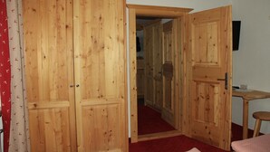 Ein Holzkleiderschrank mit zwei Türen, ein kleiner Tisch mit Stuhl und ein rot teppichbedeckter Boden.