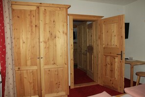 En garderob i trä med två dörrar, ett litet bord med en stol och ett rött, mattbeklätt golv.