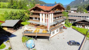 A multi-story hotel with a wooden facade, outdoor seating, and a view of the surrounding hills. - Hotel Schweizerhof (Wildschönau)