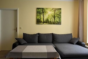 A living room with a sofa, a coffee table, and a painting of a forest.