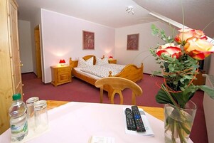 Un dormitorio con cama de madera, mesitas de noche, una silla, una mesa con un florero y un control remoto.