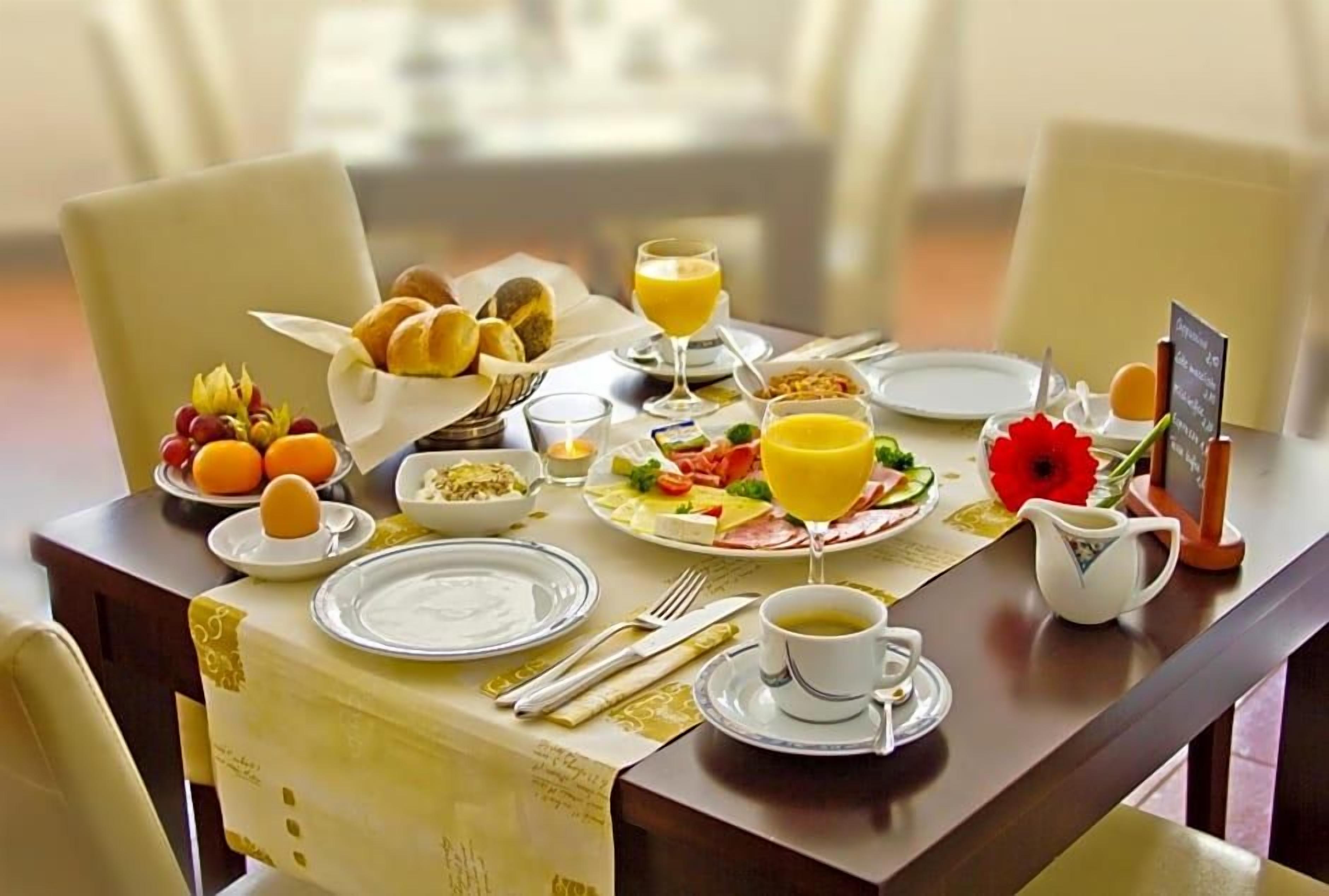 Ein Frühstückstisch ist mit Tellern, Schüsseln, einer Karaffe und einer Speisekarte gedeckt.