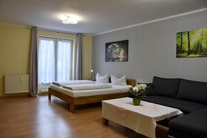 Un dormitorio con una cama, una mesita de noche con un jarrón, un sofá, una ventana con cortinas y un radiador.
