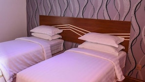 A hotel room with two single beds, each with a wooden headboard and white bedding. The walls have a wavy pattern wallpaper. - Sunset Stay Maldives (Thinadhoo)