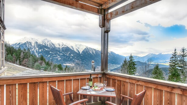 A wooden deck with a table set for two, overlooking a mountainous landscape. - Landgasthof Ropferhof (Telfs)