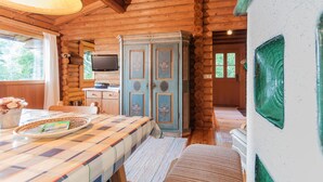 A log cabin interior with a wooden ceiling, a dining table with a placemat, a cabinet with floral designs, and a television on a wooden stand. - Landgasthof Ropferhof (Telfs)