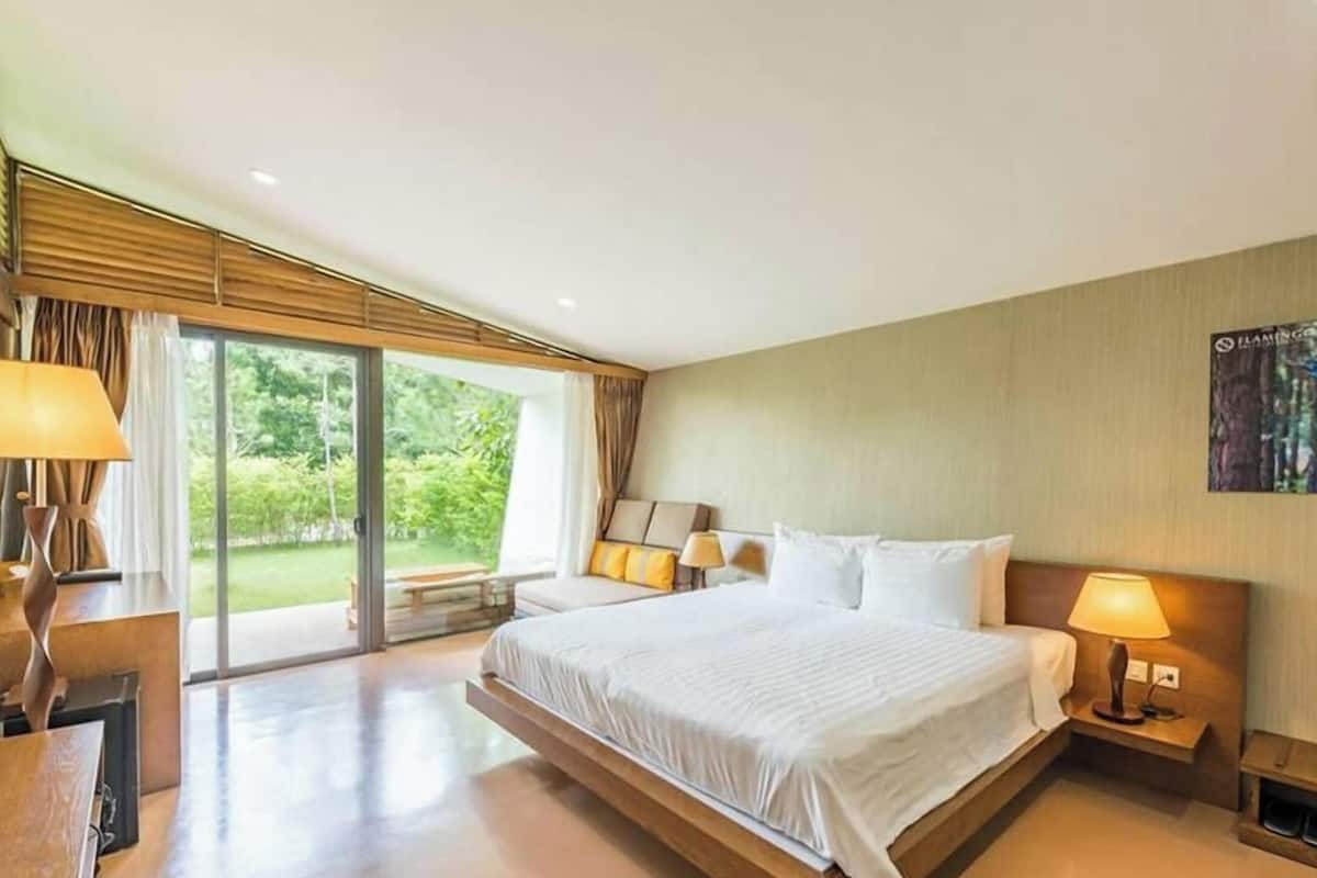 Ein modernes Hotelzimmer mit einem großen Bett, zwei Nachttischlampen, einem Holz-Kopfteil und einem großen Fenster mit Vorhängen.
