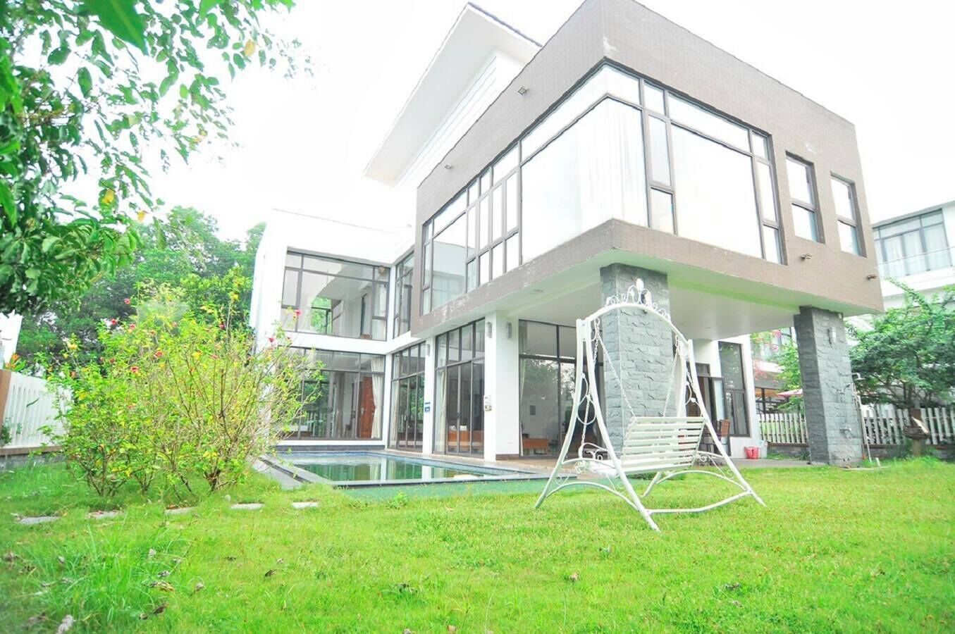 A modern two-story house with a large glass window, a swimming pool, and a garden.