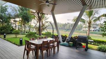 Enjoy al fresco dining under a shaded roof, surrounded by lush greenery and a serene water view.