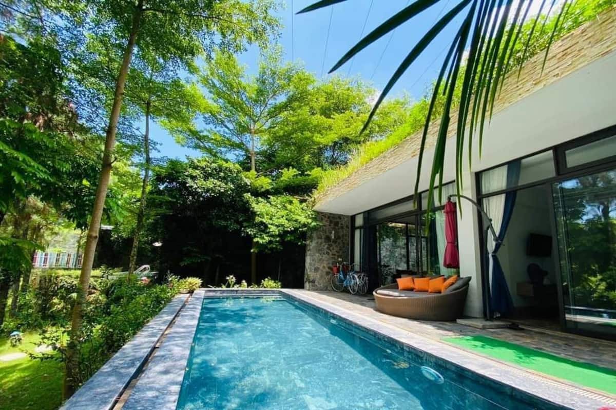 Ein moderner Poolbereich im Freien mit einer Steinwand, einer Glastür und einer Sitzecke mit Kissen.