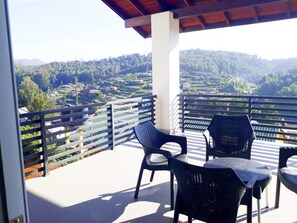 A balcony with two chairs and a table, overlooking a valley with houses and greenery. - J's Villa (Nuwara Eliya)