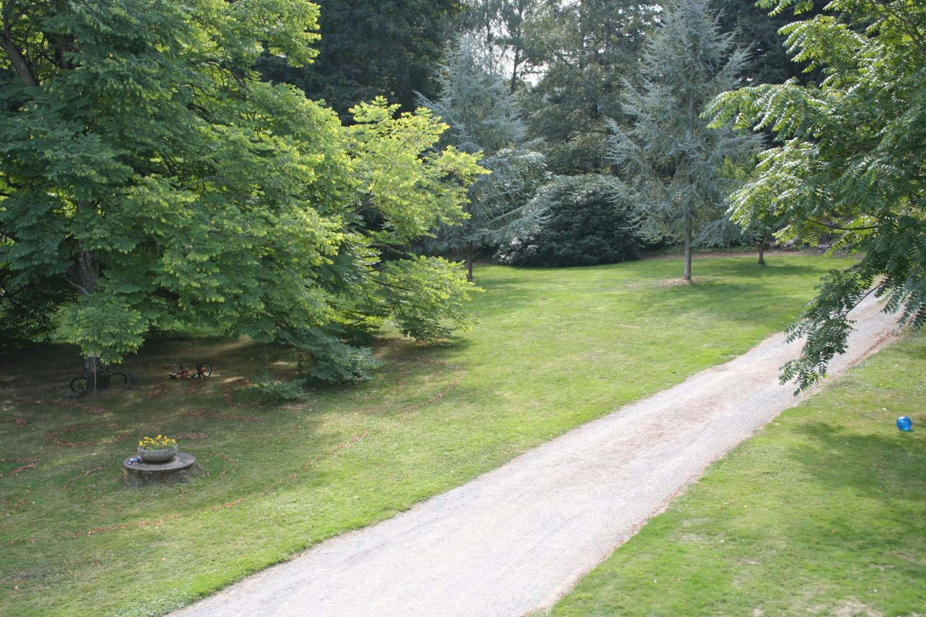 Un jardin bien entretenu, avec un chemin de gravier, entouré d’arbres et d’arbustes verdoyants.