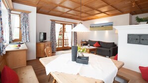 A cozy room with a wooden ceiling, a dining table with a white tablecloth, a sofa, and a television on a wooden cabinet. - Ferienwohnungen Zum Sommerfrischler (Seehausen am Staffelsee)