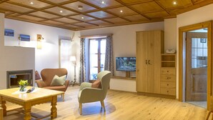 A living room with a wooden ceiling, a television, a sofa, a chair, and a table. - Ferienwohnungen Zum Sommerfrischler (Seehausen am Staffelsee)