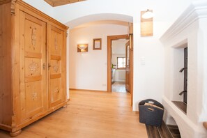 A hallway with wooden flooring, a large wooden wardrobe, a wall-mounted light fixture, and a fireplace. - Ferienwohnungen Zum Sommerfrischler (Seehausen am Staffelsee)
