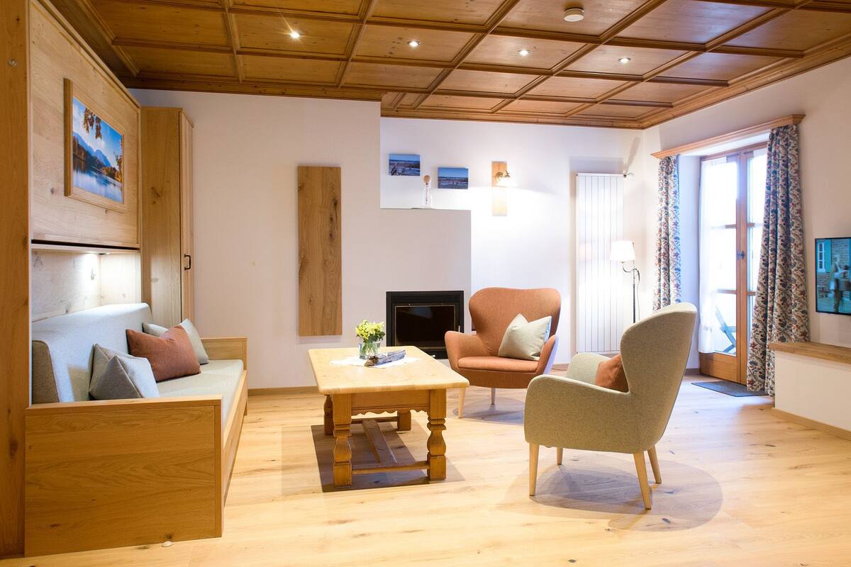 A cozy living room with a wooden ceiling, a sofa, a coffee table, and two armchairs.