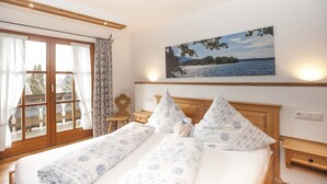 A bedroom with a large bed, a painting of a lake, and a view of a balcony. - Ferienwohnungen Zum Sommerfrischler (Seehausen am Staffelsee)