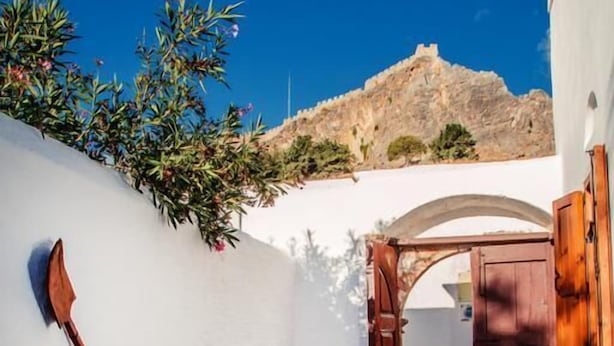 A narrow courtyard with a white wall, a wooden door, and a blue chair. - CasaLindos Theatro (Rhodes)