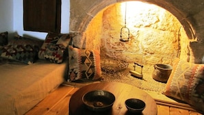 A cozy room with a stone fireplace, a wooden table with two bowls, and patterned cushions. - CasaLindos Theatro (Rhodes)