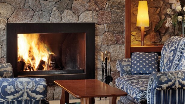 A stone wall with a fireplace, blue patterned furniture, and a table. - Hostal Piteus (Sant Llorenc de Morunys)