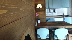 A modern kitchen with wooden walls, a microwave, and two light blue chairs. - Hostal Piteus (Sant Llorenc de Morunys)