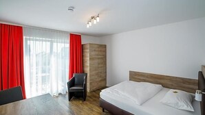 Una habitación de hotel con cama, una silla, una mesa y un ventanal con cortinas rojas.