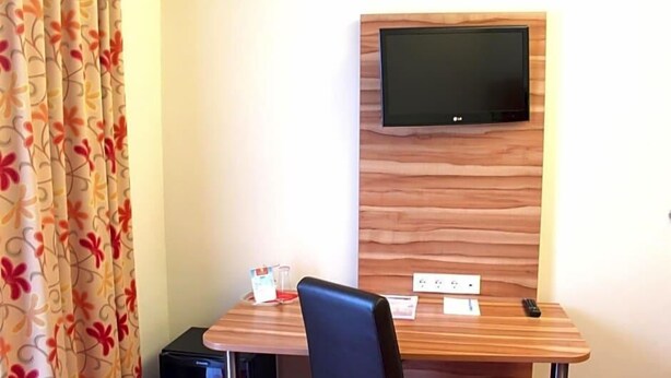 Habitación de hotel con un televisor de pared de madera, una mesita con una silla y un enchufe.