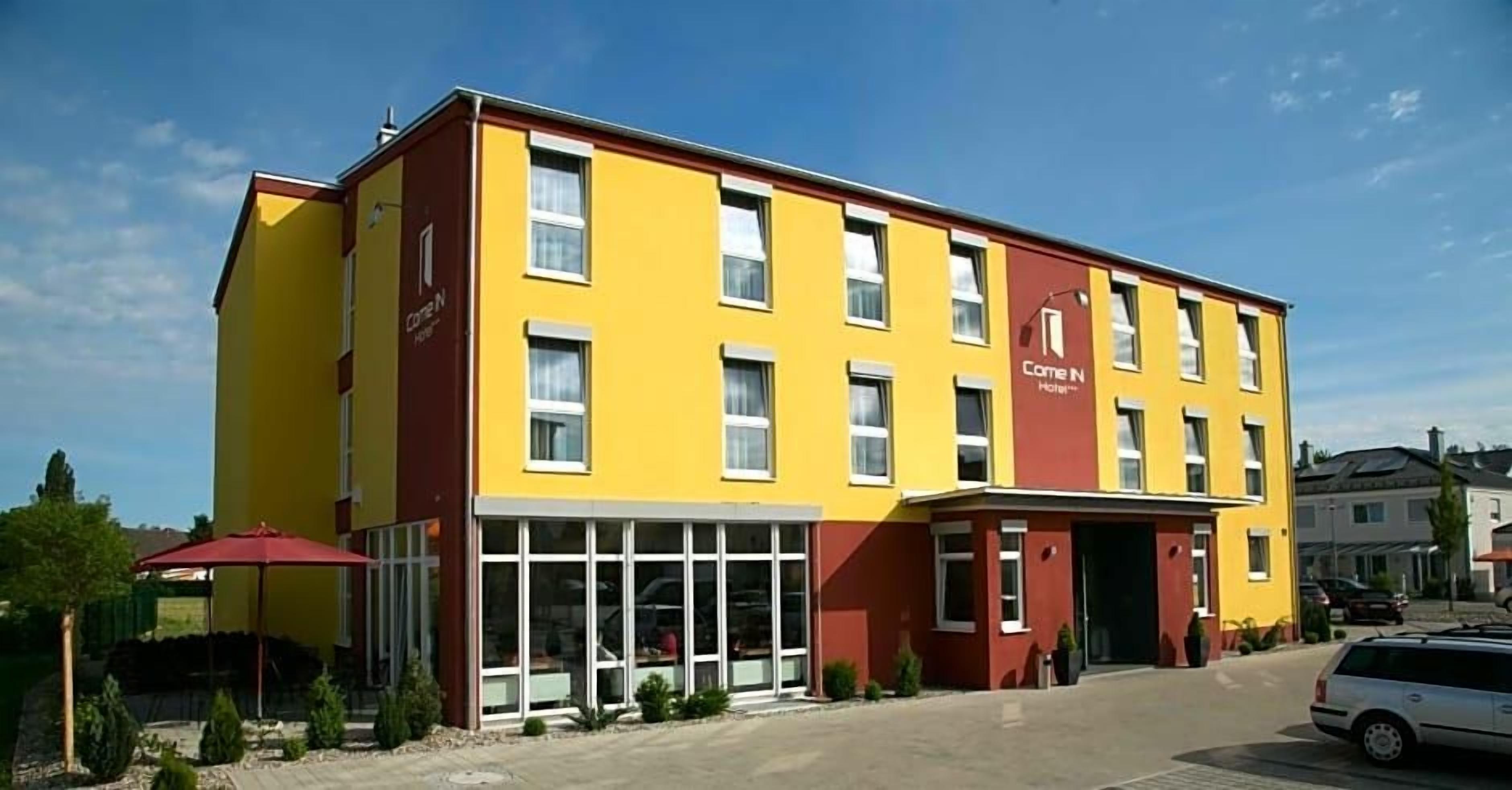 A multi-story hotel with a yellow facade, large windows, and a red entrance.