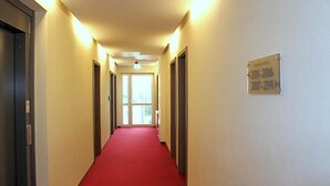Pasillo de hotel con alfombra roja, puertas a ambos lados y un letrero con los números de las habitaciones.
