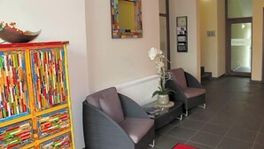 Un área de recepción con una estantería colorida, dos sillones grises, una mesita con un florero y un espejo enmarcado en la pared.