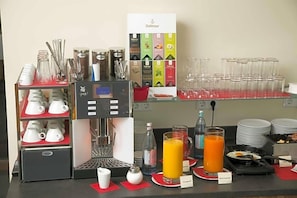 A breakfast bar with a coffee machine, tea and coffee dispensers, a variety of mugs, and a selection of breakfast items.