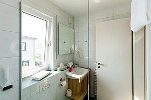 A bathroom with a window, a mirror, a sink, and a shower.
